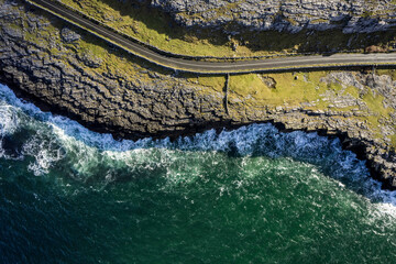 Top down view on a small road by a rough stone coastline. Rock formation and ocean water surface....