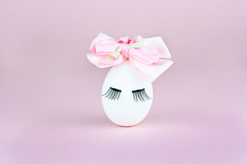 White Easter egg with eyelashes and cute bow tie headband on a delicate lavender background. Minimal Easter or food concept.