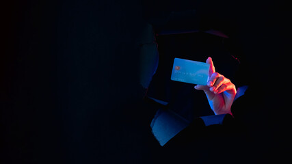 Bank scam. Money transaction risk. Personal data security. Female hand showing credit card inside black breakthrough paper hole isolated on dark night empty space banner.