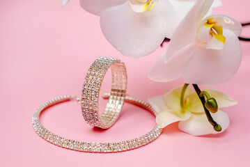 Bracelet and necklace and white orchid on pink background
