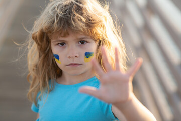 Ukraine flag on kids cheek. Little ukrainian patriot. Stop the war hand gestures. No war, stop war, russian aggression. Human protest.