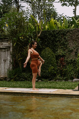 Young woman with body positive appearance practicing yoga alone on deck by the pool in tropical island of Bali, Indonesia. Sport, fitness, healthy lifestyle concept.