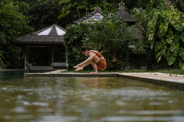 Young woman with body positive appearance practicing yoga alone on deck by the pool in tropical island of Bali, Indonesia. Sport, fitness, healthy lifestyle concept.