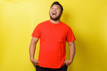 Fat asian guy laughing loudly isolated on yellow background