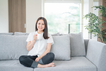 Obraz premium 部屋で飲み物を飲む女性（カメラ目線） 
