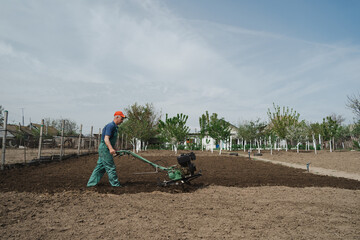 Modern farming, technology agriculture. Gardener man cultivate ground soil with tiller tractor or...