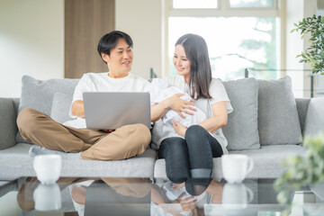 部屋でパソコンを使う赤ちゃんを抱く男女

