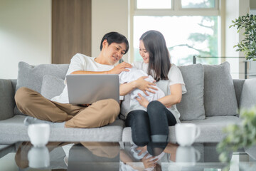 部屋でパソコンを使う赤ちゃんを抱く男女
