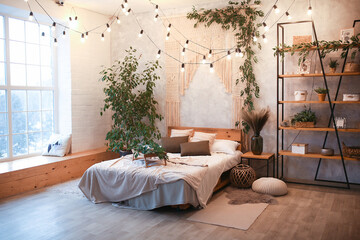 Cozy bedroom area at luxury studio apartment with a free layout in a loft style with big panoramic window and green plant.