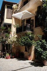 Panoramic view of a famous Mediterranean port in Greece. The image captures the historic Venetian lighthouse, crystal clear blue water, fishing boats, and old architecture under a bright summer sky,