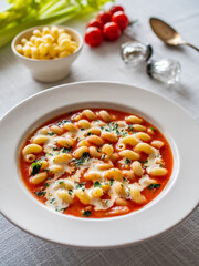 Tomato soup with cream, noodles and fresh parsley on white table
