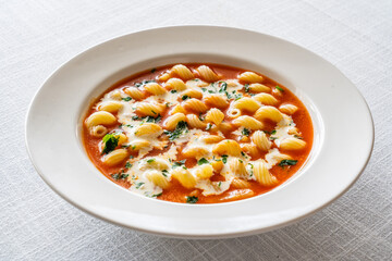 Tomato soup with cream, noodles and fresh parsley on white table
