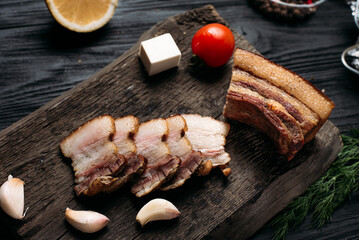 homemade hot smoked bacon, cut on an old wooden board next to vegetables and spices