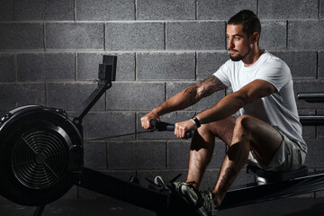 Fototapeta na wymiar Fitness young man using rowing machine in the gym