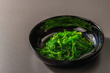 Wakame seaweed salad with sesame seeds and chili pepper in a bowl. Trendy hard light, dark shadow