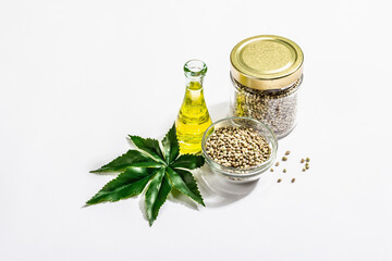 Ripe hemp seeds, oil, and artificial hemp leaf isolated on white background