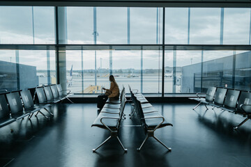 Young woman sitting at the empty airport hall. Waiting for flight. Copyspace