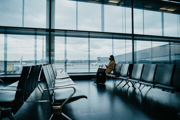 Young woman sitting at the empty airport hall. Waiting for flight. Copyspace