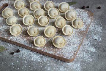 homemade dumplings on a cutting board in rows of flour, pepper and bay leaf