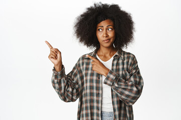 Portrait of young Black woman pointing fingers left and looking skeptical, express dislike or...