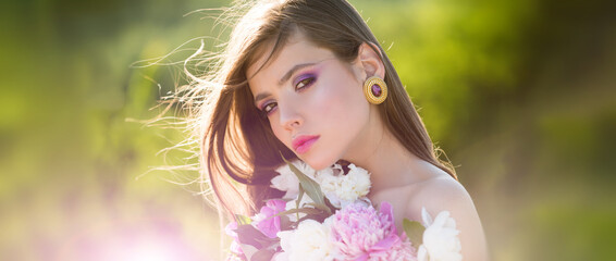 Fototapeta premium Natural beauty face. Young beautiful sexy carefree woman posing on the spring background. Summer model holding flowers in hands outdoors.