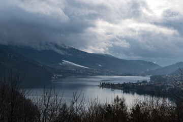 Mglisty dzień nad jeziorem Żywieckim. Chmury nad wodą, ośnieżone stoki górskie.