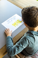 Little kid drawing Stop War on a paper. Ukraine Russia war concept.
