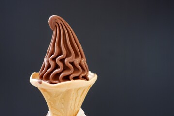 A cone of soft chocolate ice cream on dark background with copy space