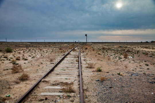 Abandoned railroad in desert. Rusted rails and wooden sleepers. Traffic light on horizon. Blue cloudy sky and sun.