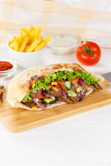 Döner Kebab Doner Kebap slice fast food in flatbread with French Fries on a wooden board portrait...
