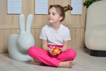 Cute little girl with ponytails holding easter painted eggs (colored or dyed eggs) in hands and sitting on floor.

Kid holding orange and pink eggs and looking aside in pink pants and white t-shirt. - Powered by Adobe
