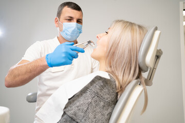 woman patient in dental clinic. A dentist in blue latex gloves removes her tooth with buccal...