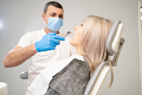 woman patient in dental clinic. A dentist in blue latex gloves removes her tooth with buccal retractor and forceps.