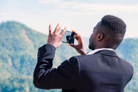 Elegant african businessman taking a photo of mountain and view of nature  with his smartphone