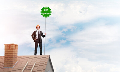 Businessman in suit on house top with ecology concept signboard. Mixed media