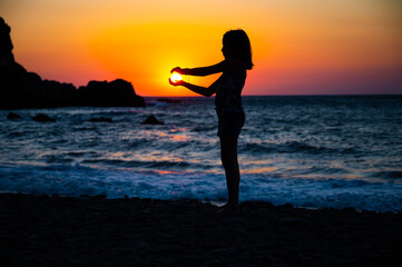 Fototapeta na wymiar Silhouette of a child holding sun in hand on a beach.
