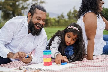 Indian parents having fun at city park playing with wood toys with their daughter - Main focus on father eye