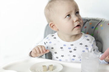 A child in a child seat in pajamas with stars drinks healthy yogurt against the background of a white wall.