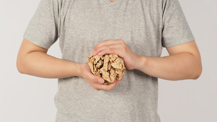The man's hand is mauling crumpled brown paper ball on white background. He wears a grey t-shirt.