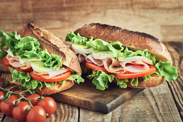 Two fresh sandwiches with ham on wooden table. Sandwich with ham tomato salad and mozzarella cheese on wooden table. Sandwich close up.