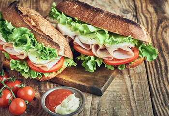 Two fresh sandwiches with ham on wooden table. Sandwich with ham tomato salad and mozzarella cheese on wooden table. Sandwich close up.