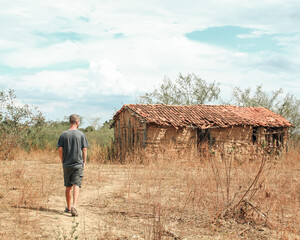 homem caminhando em frente a casa de taipa abandonada