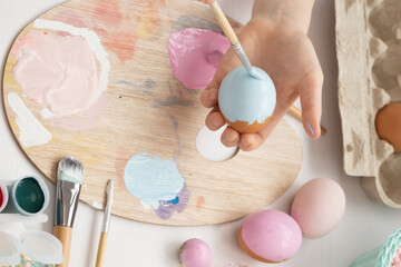 Fototapeta na wymiar Preparation for Easter. The child is holding a large egg in his hands. Pastel shades on the palette. A child's hand paints an egg light blue with a brush. Happy Easter