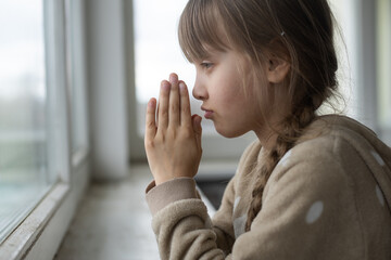 little girl praying near the window.