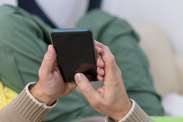 A mature man using a smart phone lying on a sofa and making internet shopping. Internet and technology,