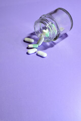 Vertical shot. Medicines, in pills on the light mauve background and in a small glass container. Copy space.
