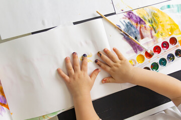 A little boy paints with watercolor paints on a table.