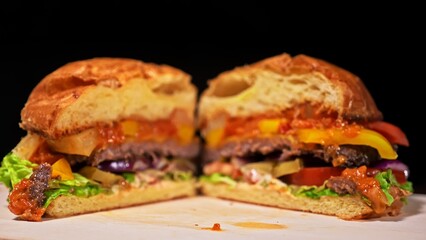 Cut craft burger is cooking on black background in black food gloves. Consist: red sauce salsa, lettuce, red onion, pickle, cheese, chilli green pepper, air bun and marbled meat beef. Not made ideal