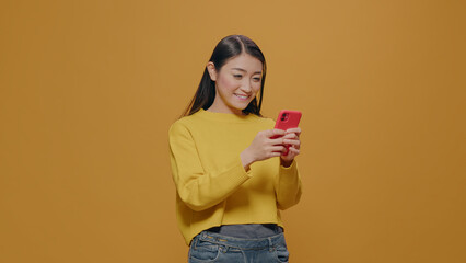 Smiling person using smartphone and typing message on touch screen. Young adult holding mobile phone to browse internet and use social media app, standing over isolated background.