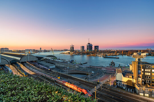 Amsterdam central station and IJ river at sunset with many different trains on the platforms